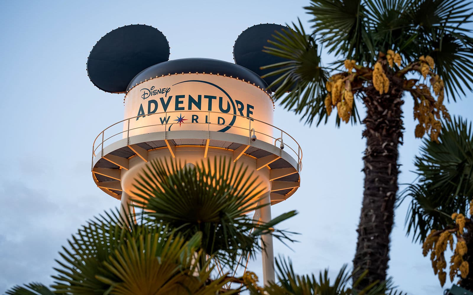 Torre Disney Adventure World con orecchie di Topolino, illuminata tra palme al crepuscolo.