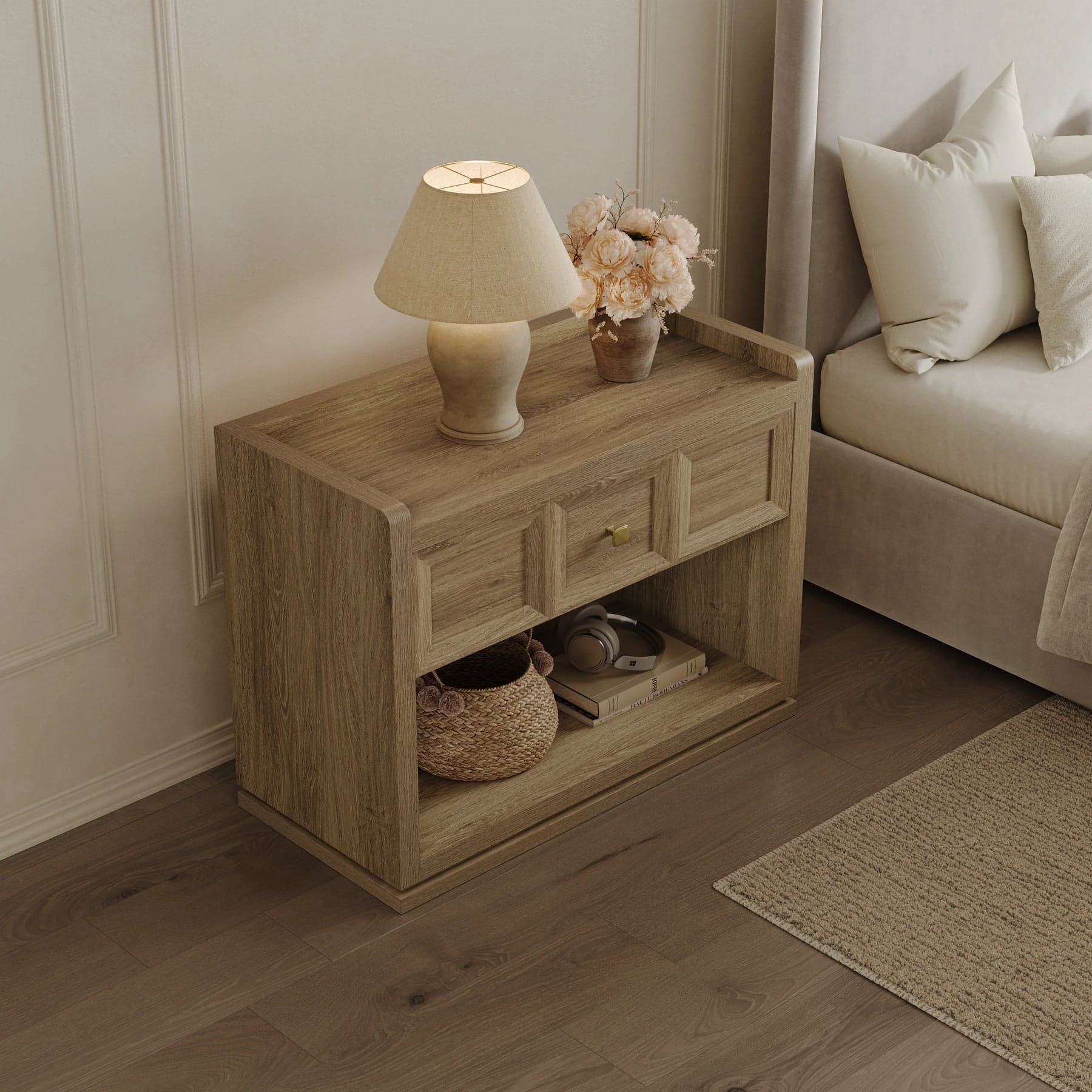 Comodino in legno chiaro con lampada e fiori accanto a un letto dai toni neutri.