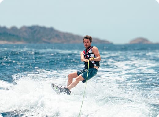 Uomo che fa wakeboard tra le onde del mare azzurro con montagne sullo sfondo.
