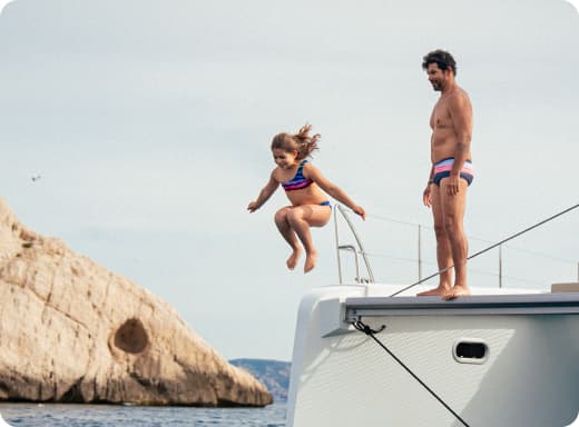 Bambina che salta da una barca in mare mentre un uomo osserva dal ponte.