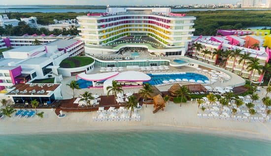 Veduta aerea di un resort colorato con piscine e palme su una spiaggia bianca.